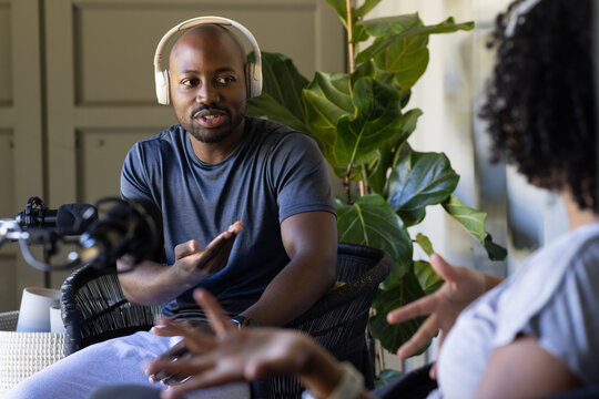 Diverse interviewer and guest conversing in cozy podcast studio with microphone and headphones