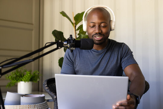 Adult man wearing white headphones and gray t-shirt, speaking into boom microphone with laptop