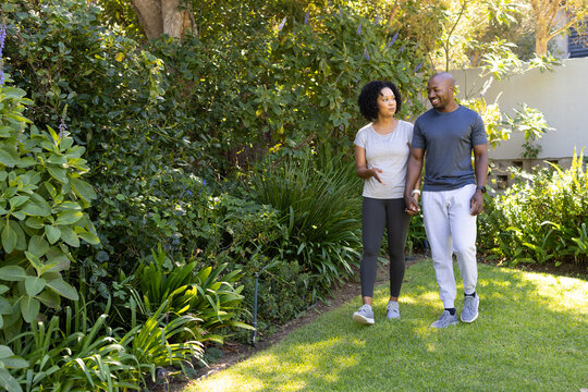 African American couple walking holding hands and talking on yard path wearing sneakers, copy space