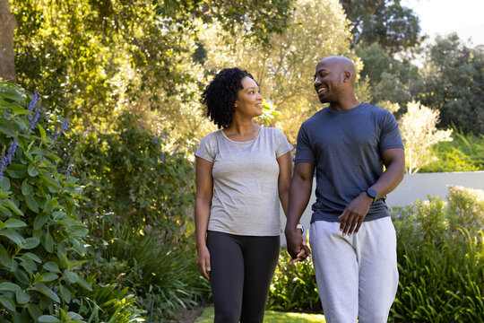 African American couple walking garden path holding hands, wearing casual clothes and smartwatch