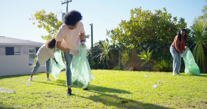 African American friends joining yard cleanup picking up litter with green bags and gloves
