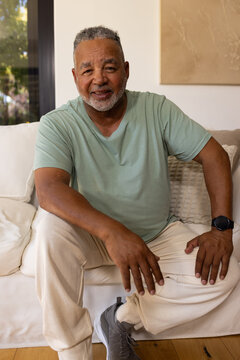 Senior African American man sitting on white sofa with green tee, black watch, pillow, window view