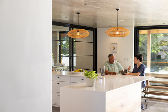 Couple mature man and woman sitting at open-plan kitchen island, gesturing near coffee press