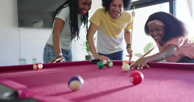 African American friends leaning at red-felt pool table, shooter striking cue ball, playing pool