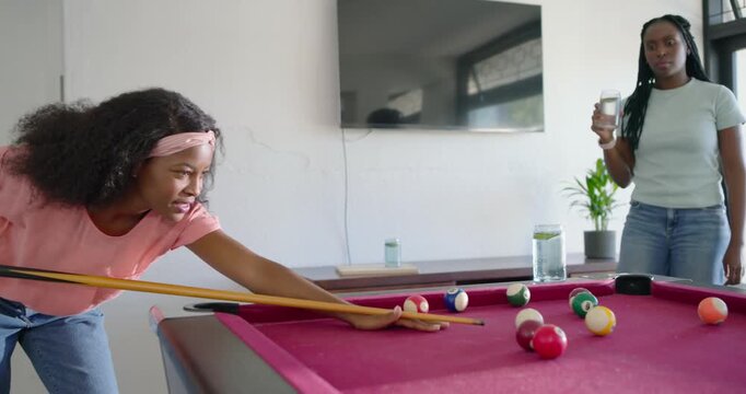 African American friends home watching woman in pink lining up, shooting to score on red-felt table