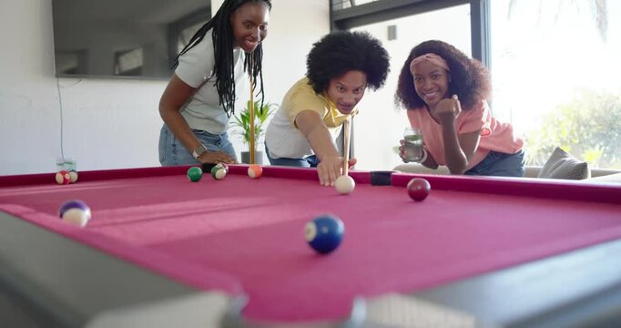 Friends studying pink felt pool table balls for game at home, man tapping cue, cheering
