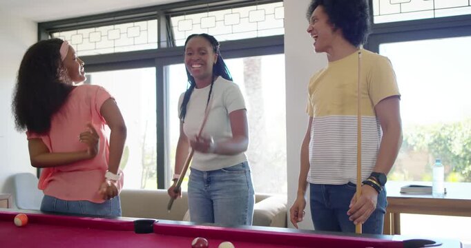 Diverse friends teasing encouraging center woman bridging striking cue ball for fun at pool table