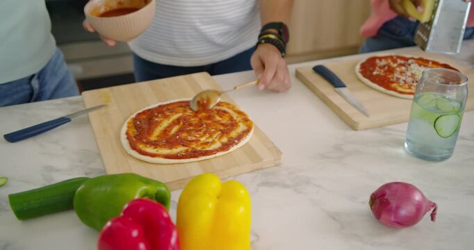 African American trio preparing pizzas for dinner spreading sauce grating cheese on kitchen counter