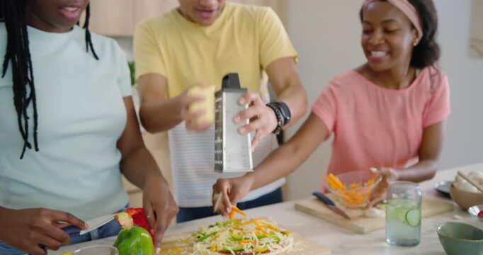 African American friends starting prep, chopping peppers and grating cheese over pizza on counter