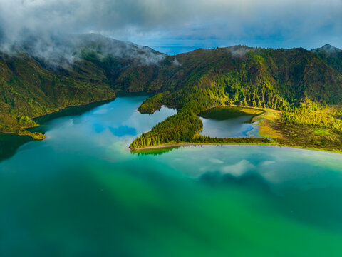 Aerial view of Lagoa do Fogo crater lake surrounded by lush green volcanic mountains and misty clouds Agua de Alto, Azores, Portugal.