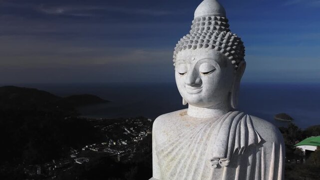 Close drone portrait of Big Buddha with island backdrop framing statue profile and distant blue sea which emphasizes texture and contemplative expression. Perfect for cultural and travel narratives.
