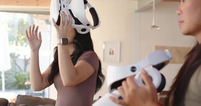 Diverse female friends getting ready, raising and aligning white VR headset in living room to try