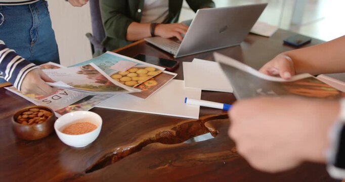 Diverse team reaching, passing, finalizing food layouts at live-edge table while laptop user typing