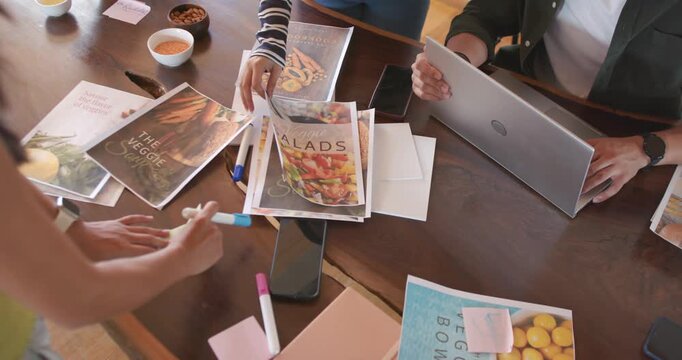 Getting proofs, Diverse team arranging SALADS, VEGGIE SOUP on wood table for laptop review