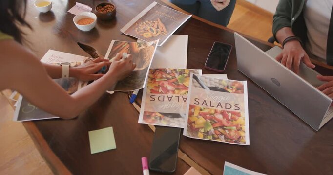 Diverse coworkers presenting new prints, annotating SALADS brochures at wooden table for redesign