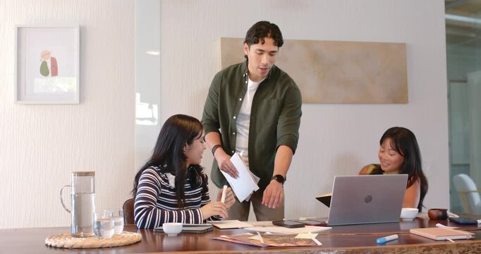 Diverse coworkers watching standing African man opening binder, flipping pages on table for review