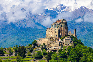 Fototapeta premium Sacra di San Michele abbey perched on Mount Pirchiriano at the entrance of the Susa Valley in spring, with the still snow-capped Alpine peaks emerging through the clouds in the background