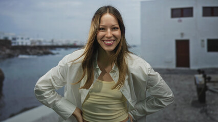 Fototapeta premium Woman smiling with hand on hip on street beside seaside promenade, leaning forward in a casual tank top; carefree joy.