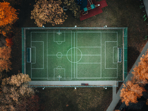 Aerial view of a green multipurpose sports field surrounded by colorful autumn trees and a small playground in Elk, Warmian-Masurian Voiv, Poland.