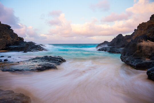 Long exposure of waves rushing across golden sand into Halona Beach Cove on Oahu, Hawaii.