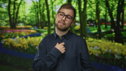 Fototapeta premium Man with hand on chest and glasses standing among tulip beds in forest park, green outdoors; contemplation.