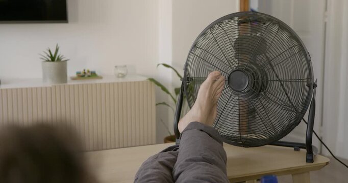 Keeping Cool: A person's feet rest in front of a fan, seeking relief from the heat, in a modern living room setting.