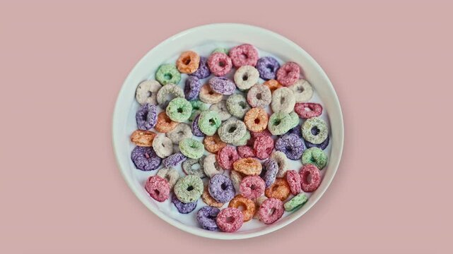 Top View of Colorful Fruit Cereal Loops in Milk on Pink Background