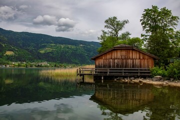 Obraz premium old boat house at Lake Ossiach with mountains cloud sky and reed grass, a famous travel destination at the Austrian region of Carinthia