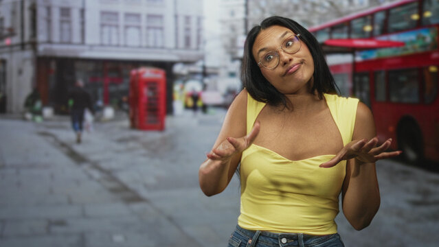Woman shrugging with palms up and slight smirk on a london street beside red doubledecker bus and phone booth; nonchalant.