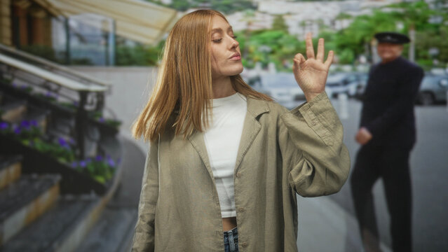 Woman redhead showing ok hand gesture with visible hand at building entrance on street near steps and parked cars; casual confidence.