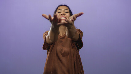 Obraz premium Young hispanic brunette woman with outstretched hands reaching toward camera in a purple studio; warm welcoming joy.