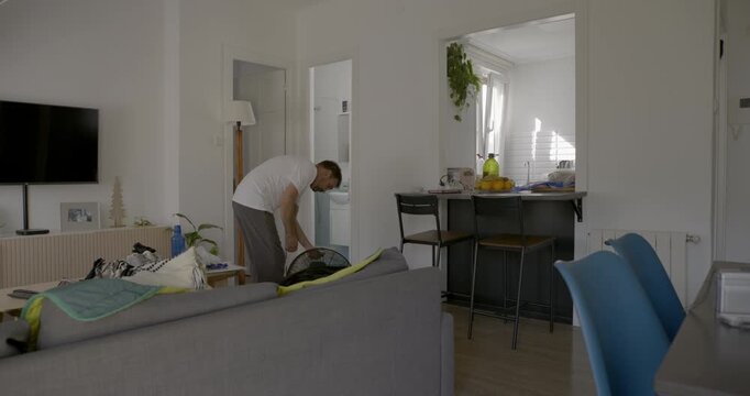 Man Cleaning Living Room: A man in casual wear is busy cleaning his living room, possibly vacuuming the floor, showcasing a relatable everyday chore in a home environment.