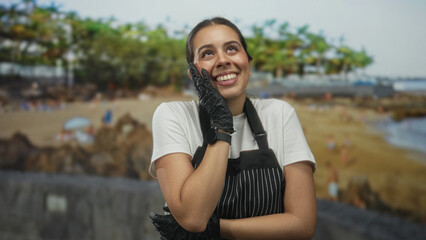 Fototapeta premium Young brunette woman wearing a pinstriped apron and black gloves, hand on chest and smiling with eyes closed in studio setting; gratitude warmth.