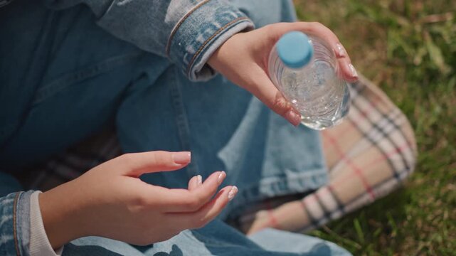 Young white woman holding crushed bottle, denim jacket on plaid blanket, slow careful hands inspecting empty water bottle, late afternoon sunlight, reflective mood about recycling and sustainability