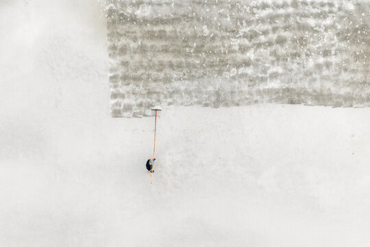 Aerial view of a worker raking salt on a vast white salt field under bright daylight in Dong Hai, Ninh Thuan, Vietnam.