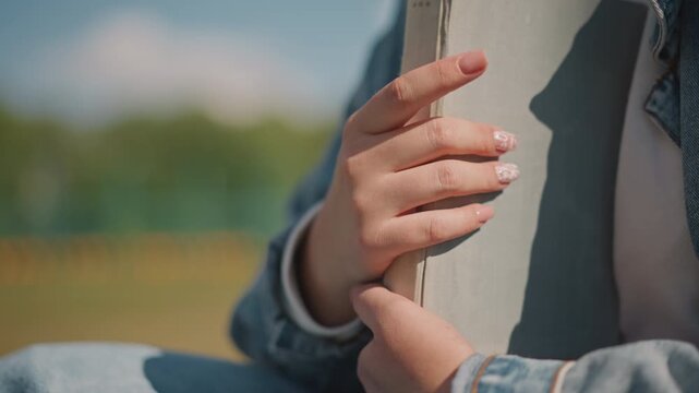 Detailed image of hands holding book gracefully. Focus on hands gripping book with refined nail artistry. Intimate depiction of wellgroomed hands clutching book with precision and elegance