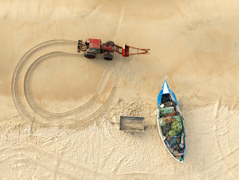 Aerial view of a red tractor creating circular tracks near a traditional blue fishing boat with nets on the sand Praia de Mira, Coimbra, Portugal.