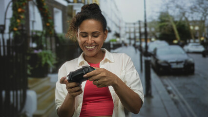 Woman smiling with bare hands holding a game controller and pressing buttons on urban street near parked cars  joy leisure play. © Krakenimages.com