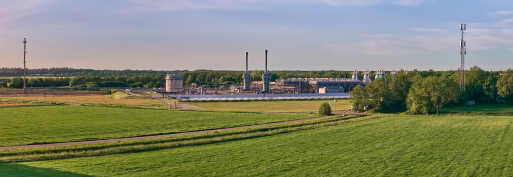 Aerial view of the NAM natural gas storage facility with industrial stacks and storage tanks surrounded by green fields and lush forests in Langelo, Drenthe, Netherlands.