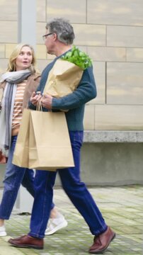 Vertical video: Stepping couple in sweaters walking courtyard holding paper bags and coffee talking