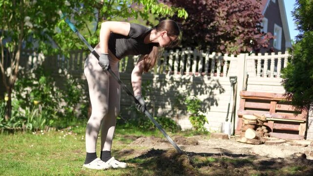 A woman is working in the garden. A woman is raking the lawn. A woman is raking the garden of a private house.