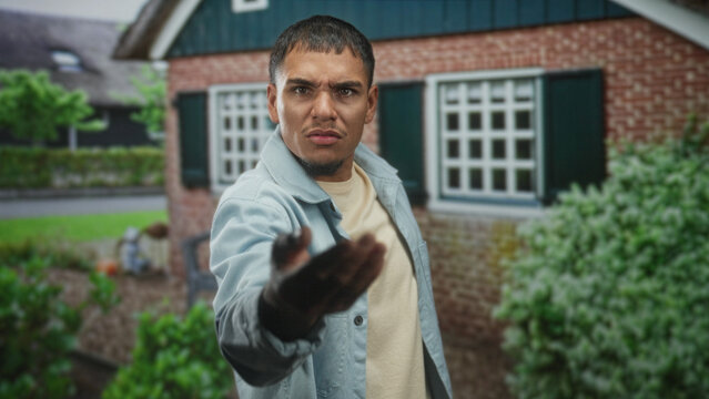 Man pointing finger with outstretched hand at camera in front of brick building entrance; accusation anger.