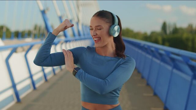Happy young woman in sportswear flexing her bicep after outdoor workout, 4K