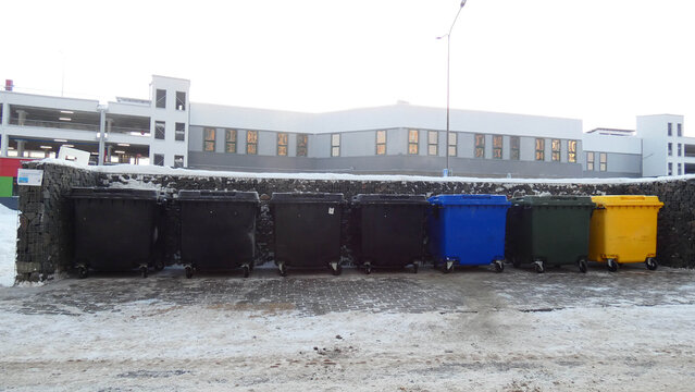 Row of trash bins at a recycling station near a building during winter