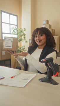 Woman holds a cardboard package and points to the shipping label while smiling at a building counter; small business confidence.