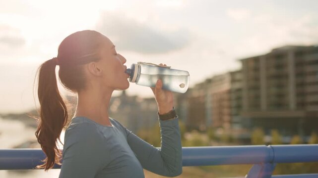 4K footage of young sporty woman drinking water during outdoor running