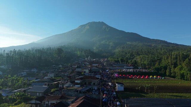 Aerial view of a large crowd gathered for Eid Al-Adha prayer in a village at the foot of a majestic mountain in Kecamatan Kalikajar, Jawa Tengah, Indonesia.