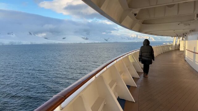 Female Cruise Ship Traveler Walks on Deck Alone in Antarctica. Beautiful Light Epic Scene Wearing Black Coat Parka Hood and Gloves.