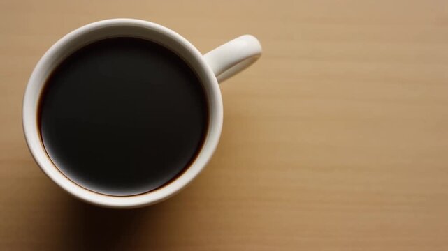 Static top down shot of coffee cup sitting on wooden table with subtle lateral shift and steady overhead perspective during morning routine