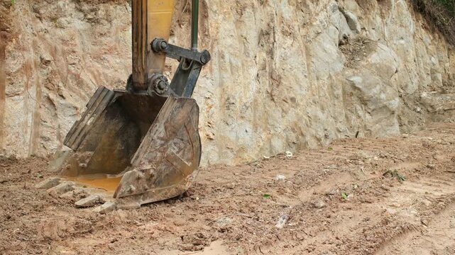 Excavator bucket with mud and soil at construction area with empty space on right side for text or advertising. Industrial machinery closeup outdoors.